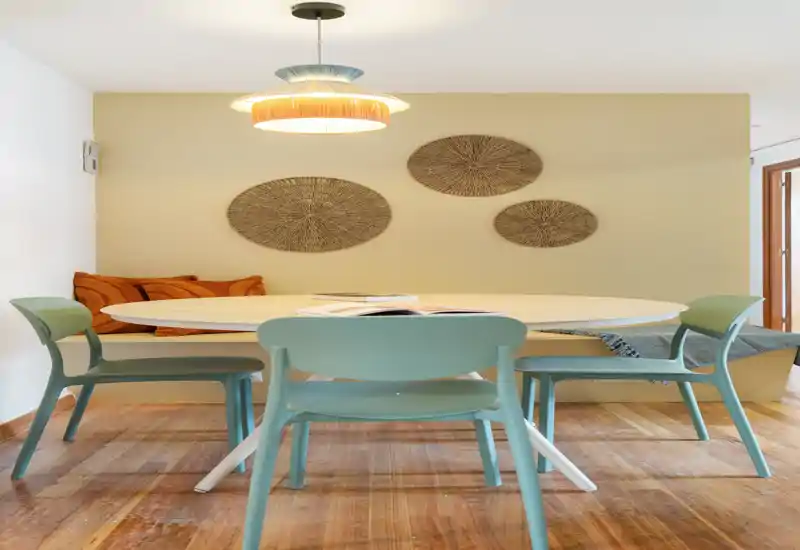 Coin repas lumineux et soigné avec table ronde, chaises pastel et éléments décoratifs muraux, idéal pour des repas conviviaux.