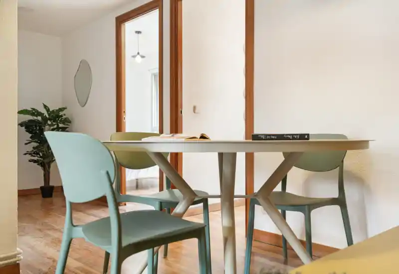 Coin repas moderne et lumineux avec une table ronde et quatre chaises pastel sur un sol en bois chaleureux — simple, élégant et accueillant pour le petit-déjeuner ou un repas décontracté.