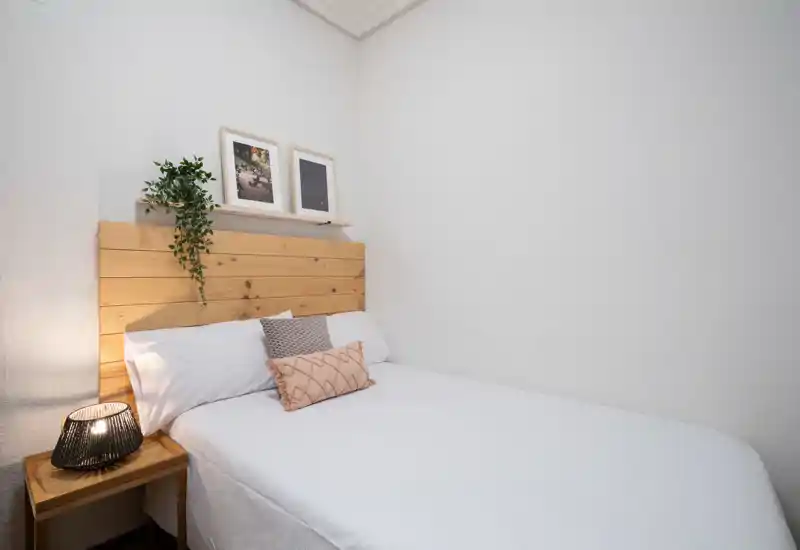 Dormitorio compacto y bien decorado con cabecero de madera, cojines decorativos y una lámpara de mesilla que crea un ambiente acogedor.