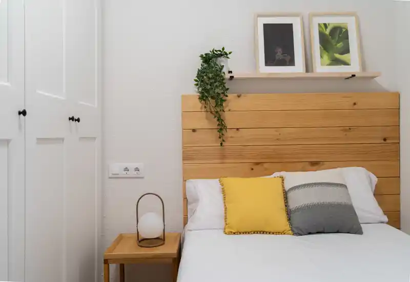 Dormitorio luminoso y acogedor con cabecero de madera, cojines decorativos y mesita de noche — un rincón minimalista ideal para descansar.
