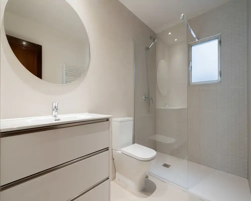 Bagno moderno e luminoso con doccia a filo pavimento con parete in vetro, mobile lavabo e WC — design pulito e contemporaneo con toni neutri e buona luce naturale.