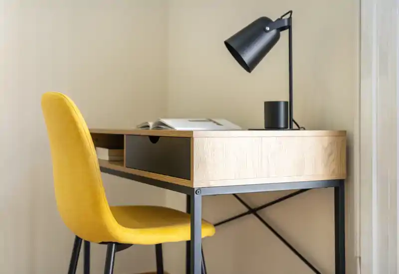 Rincón de escritorio luminoso y moderno con mesa de madera, lámpara negra y una silla tapizada amarilla vibrante — ideal para teletrabajo o zona de estudio.