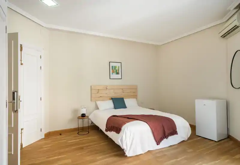 Bright, minimal bedroom with a wooden headboard, white bedding and a warm throw; simple, modern styling ideal for rental photos.