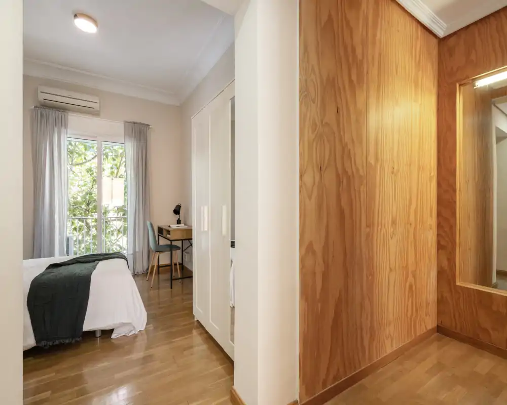 Bright, styled bedroom with a comfortable double bed, a desk by the window and warm wooden accents creating a cozy atmosphere.