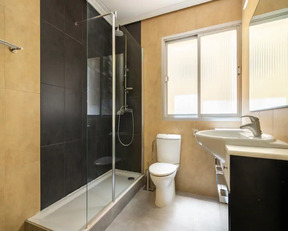 Modern bathroom with walk-in shower, glass screen, toilet and wall-mounted sink; neutral tiles and ample natural light make the space bright and clean.