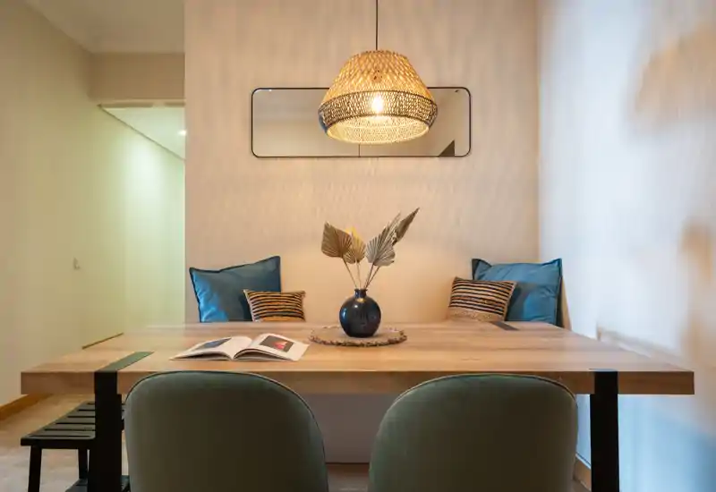 Acogedor rincón comedor con mesa de madera, sillas tapizadas, cojines decorativos y una lámpara colgante cálida — perfecto para comidas íntimas o trabajar desde casa.