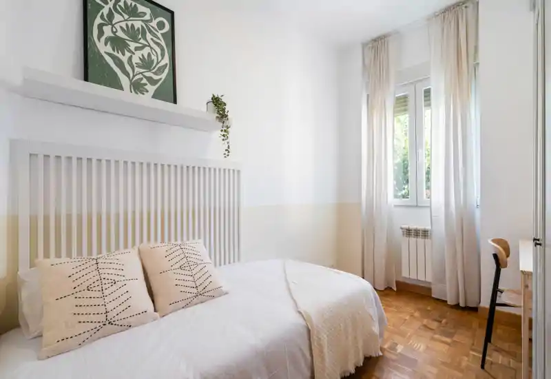 Bright, cozy bedroom with a neatly made double bed, soft neutral textiles and a window that floods the room with natural light.