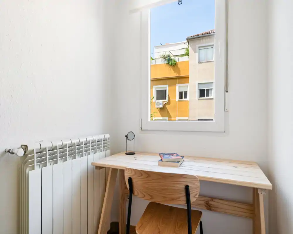Coin compact et lumineux avec un bureau et une chaise en bois sous la fenêtre — idéal comme petit espace de travail ou coin bureau lumineux.