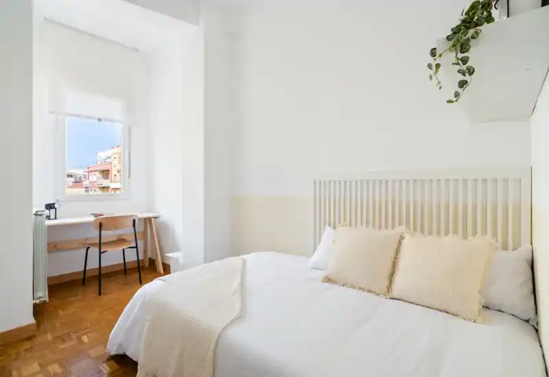 Bright, minimalist bedroom with a comfortable double bed, soft neutral linens and a small desk by the window — ideal for a restful stay or remote work.