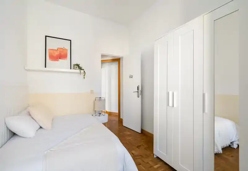 Minimal, bright bedroom with a single bed, white wardrobe and warm wooden floor — softly styled for a cozy stay.
