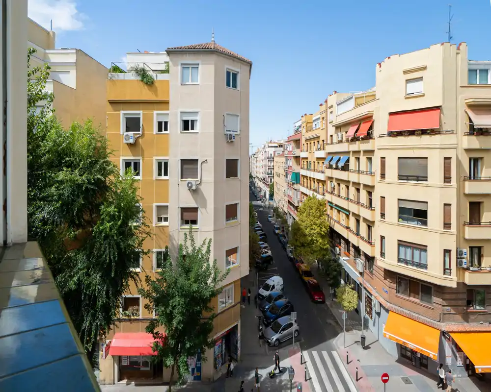 Vue de rue depuis un balcon/fenêtre montrant des immeubles, des voitures garées et des piétons sous un ciel dégagé — parfait pour illustrer l'emplacement et le quartier.