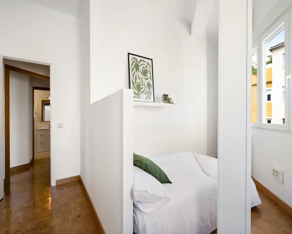 Chambre compacte et lumineuse avec un lit double bien fait, linge blanc et coussin vert en accent. La lumière naturelle et la décoration minimaliste donnent une sensation d'espace et de fraîcheur.