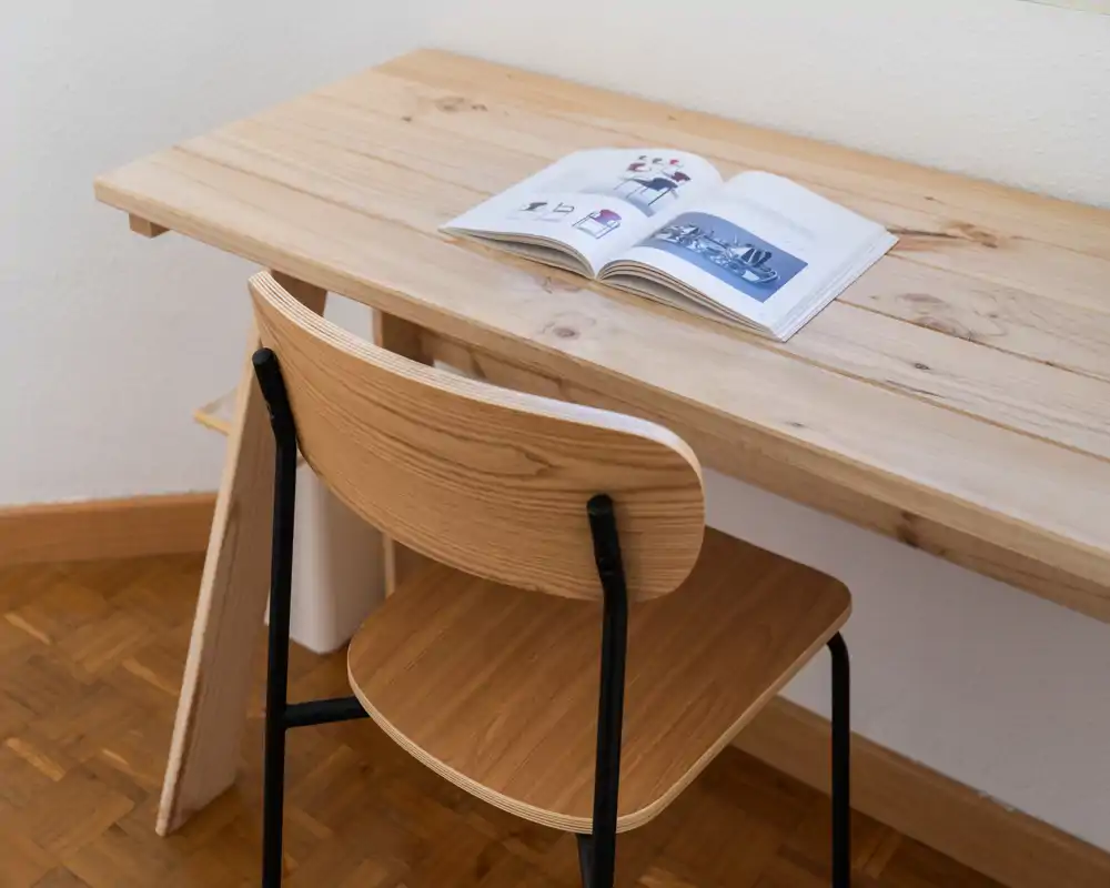 Coin minimaliste et bien éclairé avec un bureau en bois et une chaise assortie, mis en scène avec un livre ouvert — parfait pour un petit espace de travail dans le séjour.