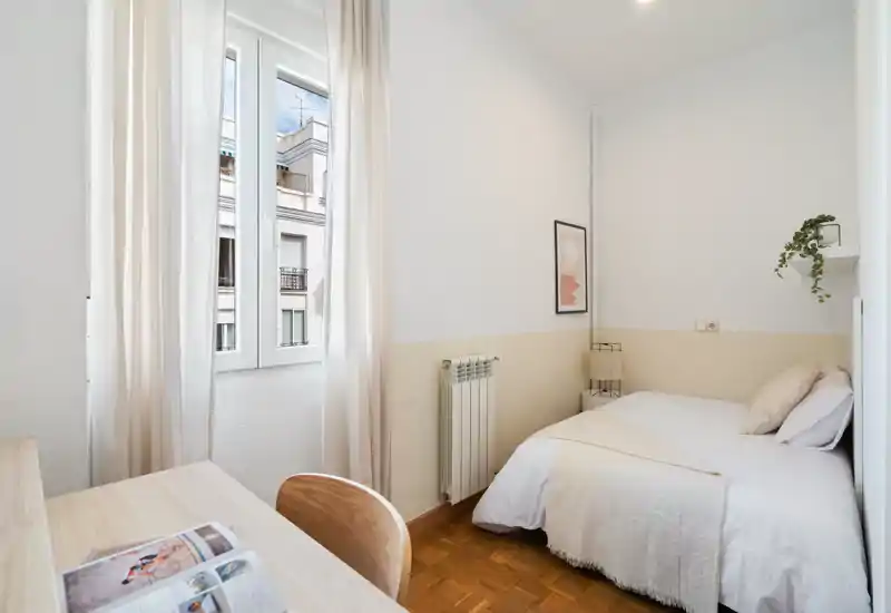 Bright, cozy single bedroom with a neatly made bed, soft neutral textiles and a study desk by the window—ideal for a comfortable stay.