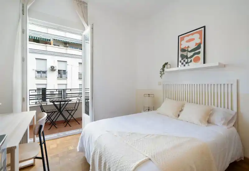 Bright, cozy bedroom with a full double bed, light textiles and direct access to a small balcony with table and chairs—ideal for morning coffee.