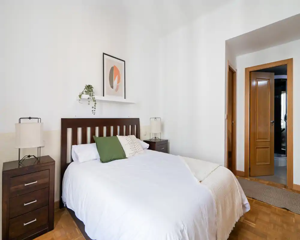 Bright, well-staged bedroom with a queen bed, wooden headboard, bedside tables and soft textiles — ideal for rental photos highlighting comfort and cleanliness.