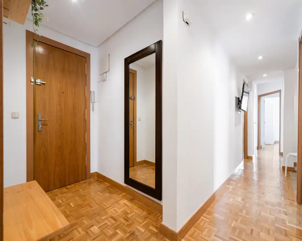 Bright, tidy entrance hallway with wooden parquet flooring, a full-length mirror and a solid wooden front door — ideal as a welcoming entry area.