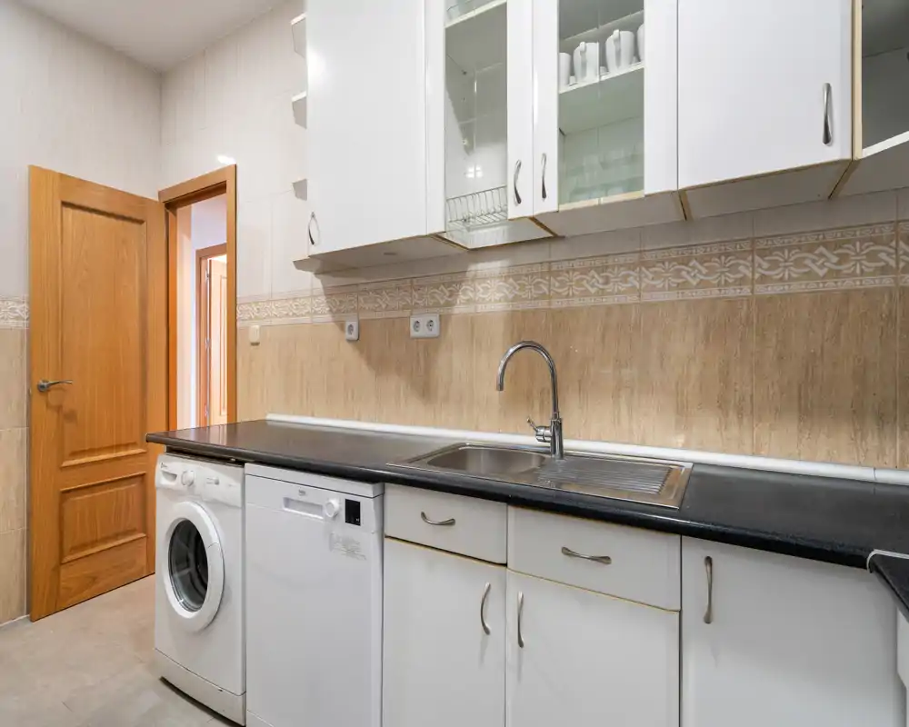 Bright, functional kitchen with white cabinetry, integrated appliances and a stainless-steel sink — clean and practical layout ideal for everyday use.