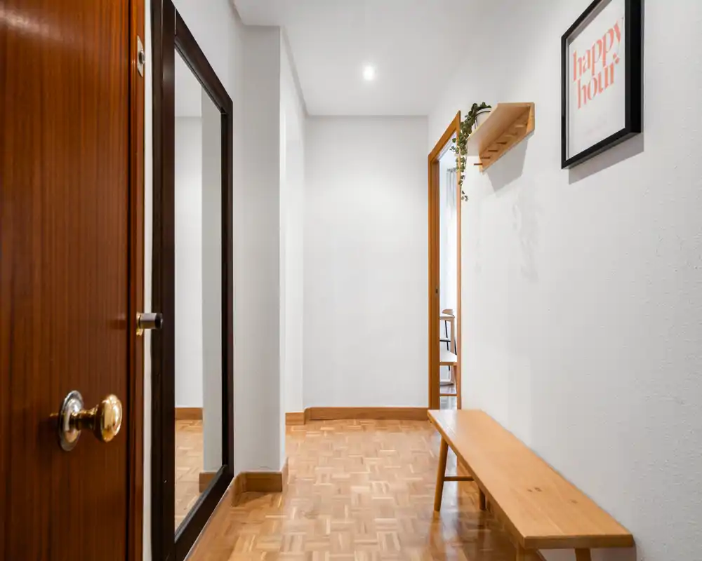 Bright, minimal entry hallway with a wooden bench, full-length mirror and parquet flooring — a welcoming and practical entrance area.