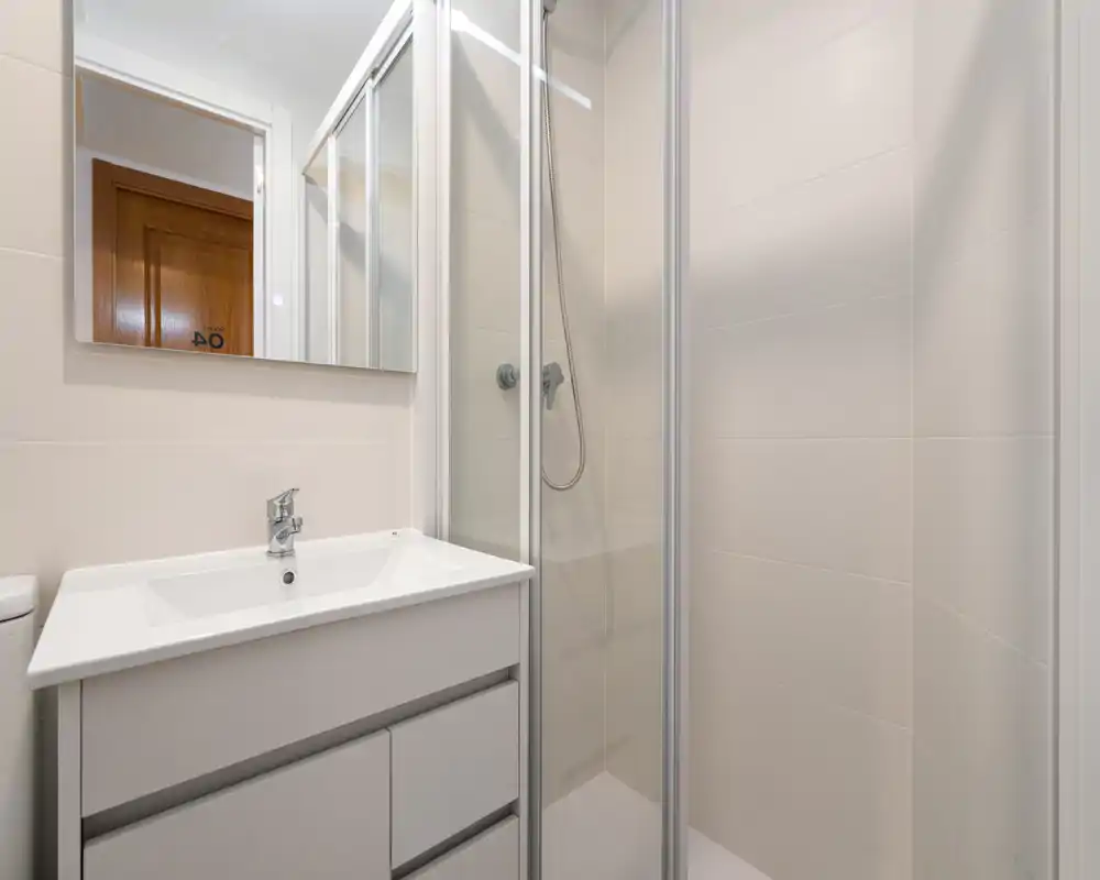 Bright, modern bathroom with a glass shower enclosure, wall-mounted shower head, and a white vanity with integrated sink and mirror.