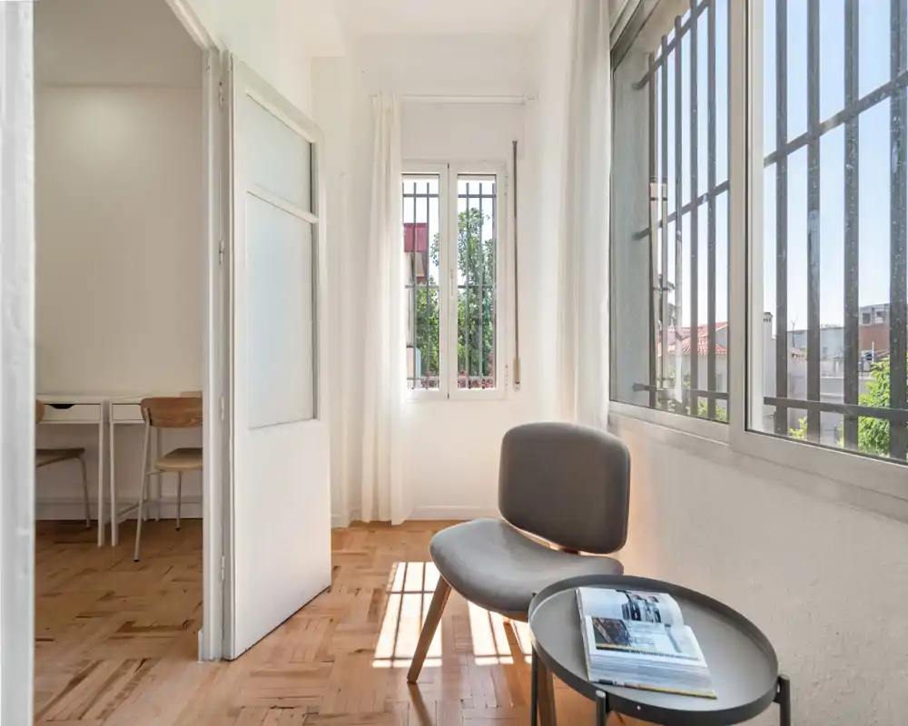 Espace de vie lumineux et minimaliste avec un fauteuil confortable près de grandes fenêtres et une petite table d'appoint — parquet moderne et ambiance aérienne.