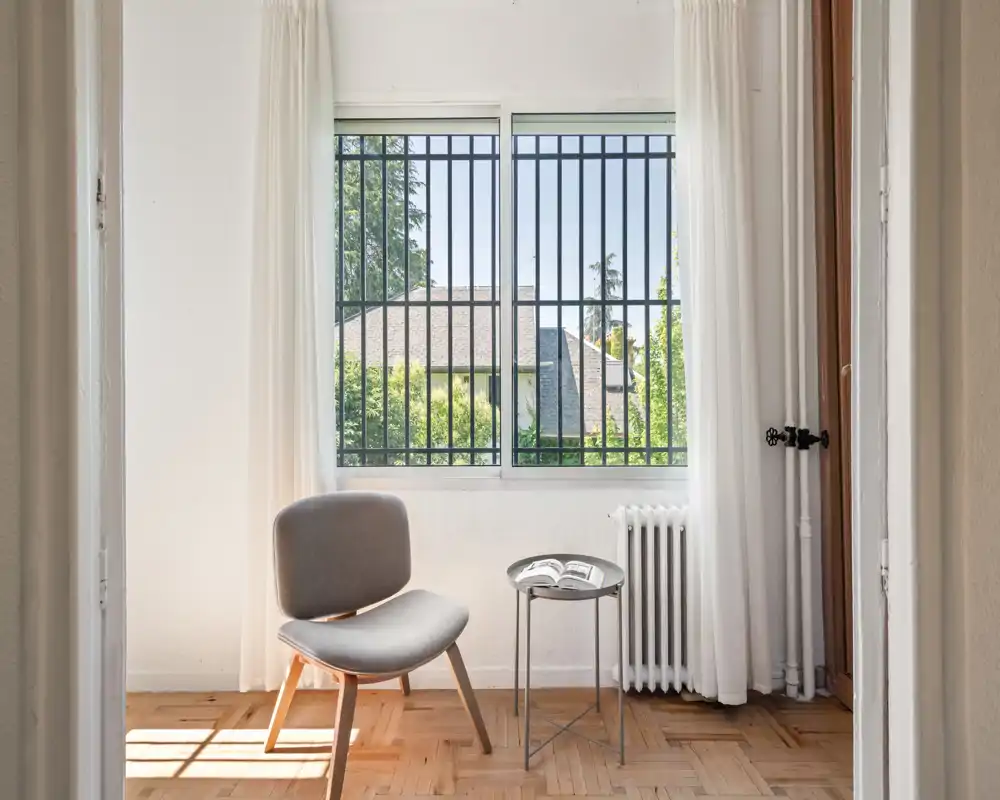 Coin salon lumineux et minimaliste avec un fauteuil confortable près d'une petite table d'appoint et une grande fenêtre qui inonde l'espace de lumière naturelle.