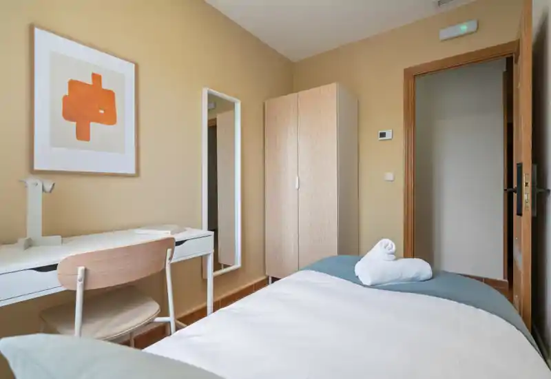 Bright, neatly styled single bedroom with a made bed, desk and wardrobe — ideal for a comfortable short stay.