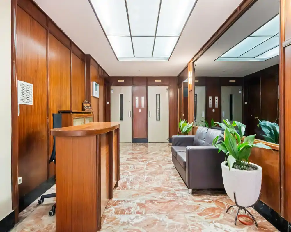Bright, well-kept building entrance or lobby with wood-paneled walls, a reception desk, seating area and decorative plants, ideal for showcasing common areas in a rental listing.
