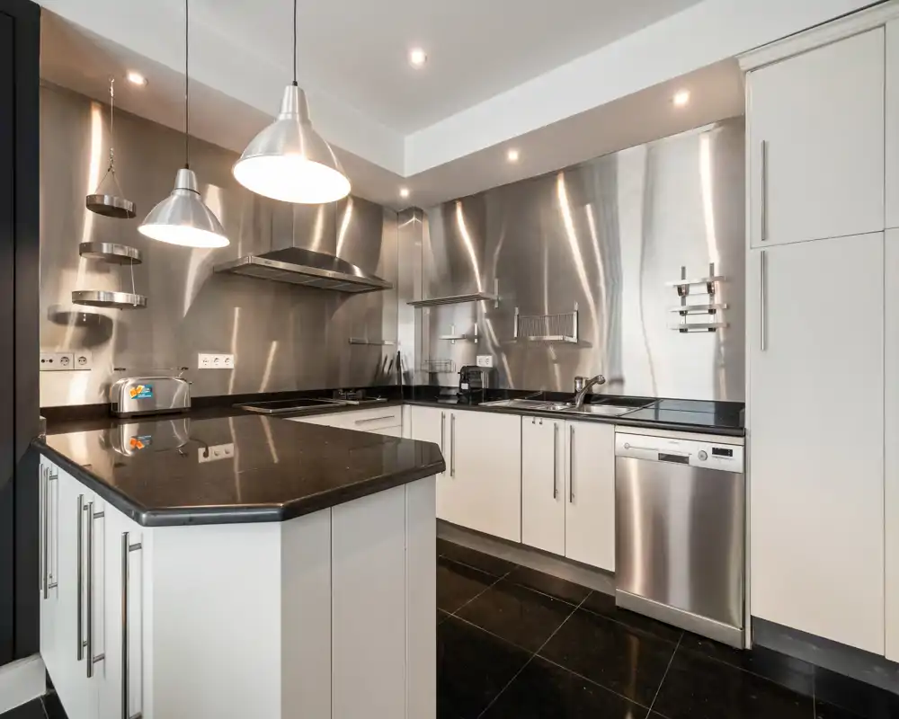 Bright modern kitchen with stainless steel backsplash, built-in appliances, island with black countertop and pendant lights — sleek, functional space ideal for rental listings.