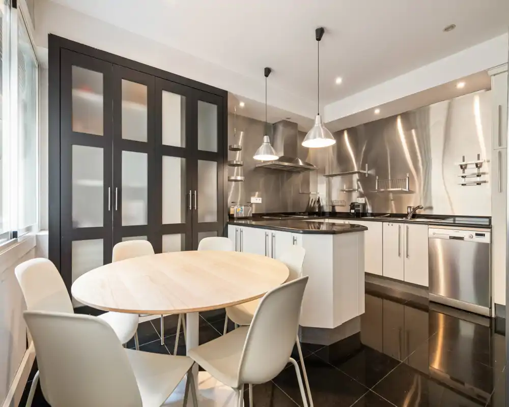 Contemporary kitchen with stainless-steel backsplash, central island and a round dining table — bright, clean and functional space for cooking and casual dining.