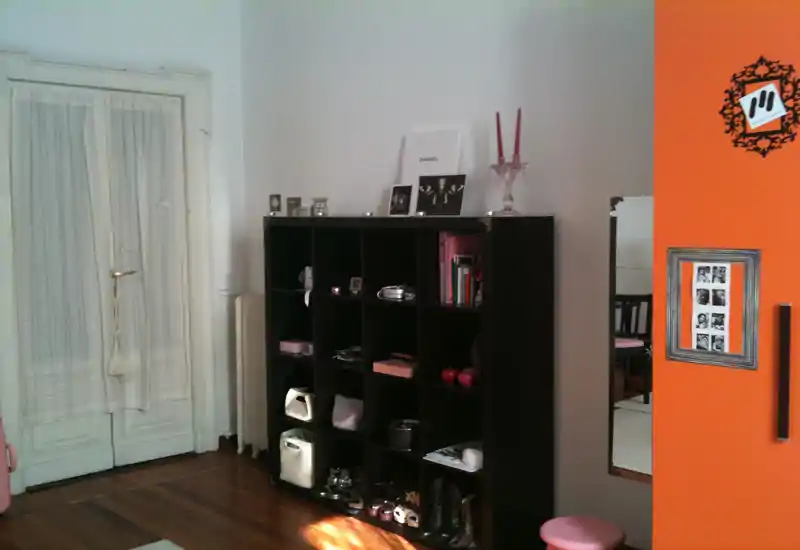 Stanza con scaffalatura e oggetti decorativi che sembra parte di una camera da letto o zona spogliatoio — luce naturale, mobile organizer e oggetti personali visibili.