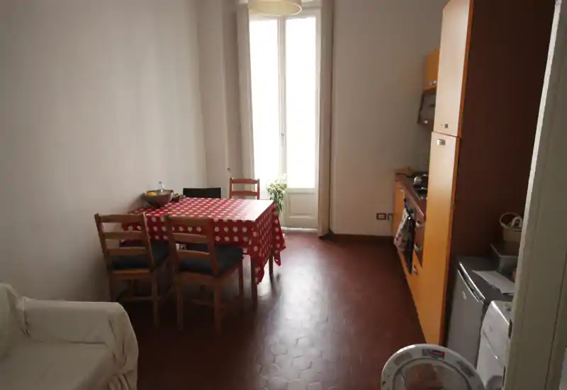 Angolo cucina con mobile cucina arancione, tavolo per quattro con tovaglia rossa a pois e una finestra alta che illumina l'ambiente.
