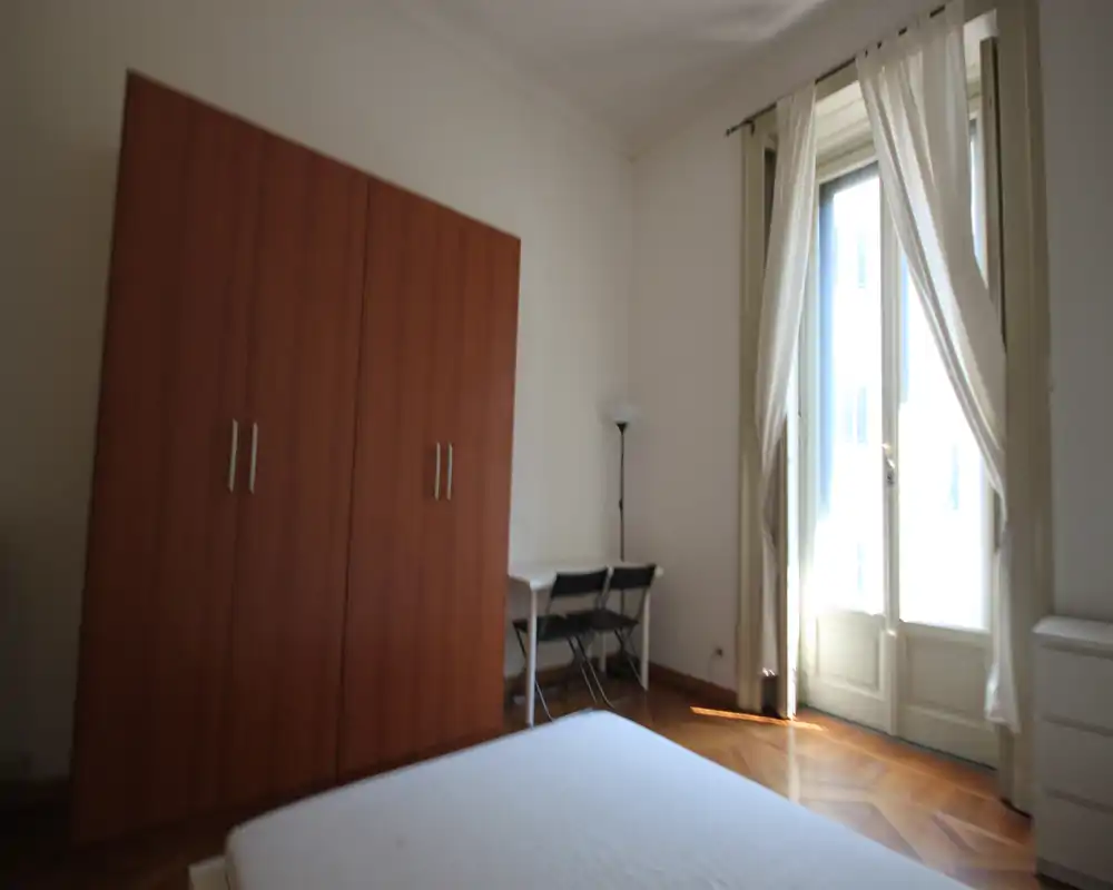 Dormitorio luminoso con gran armario, suelo de parqué y puerta-balconcín que aporta mucha luz natural; escritorio sencillo con sillas como zona de trabajo.