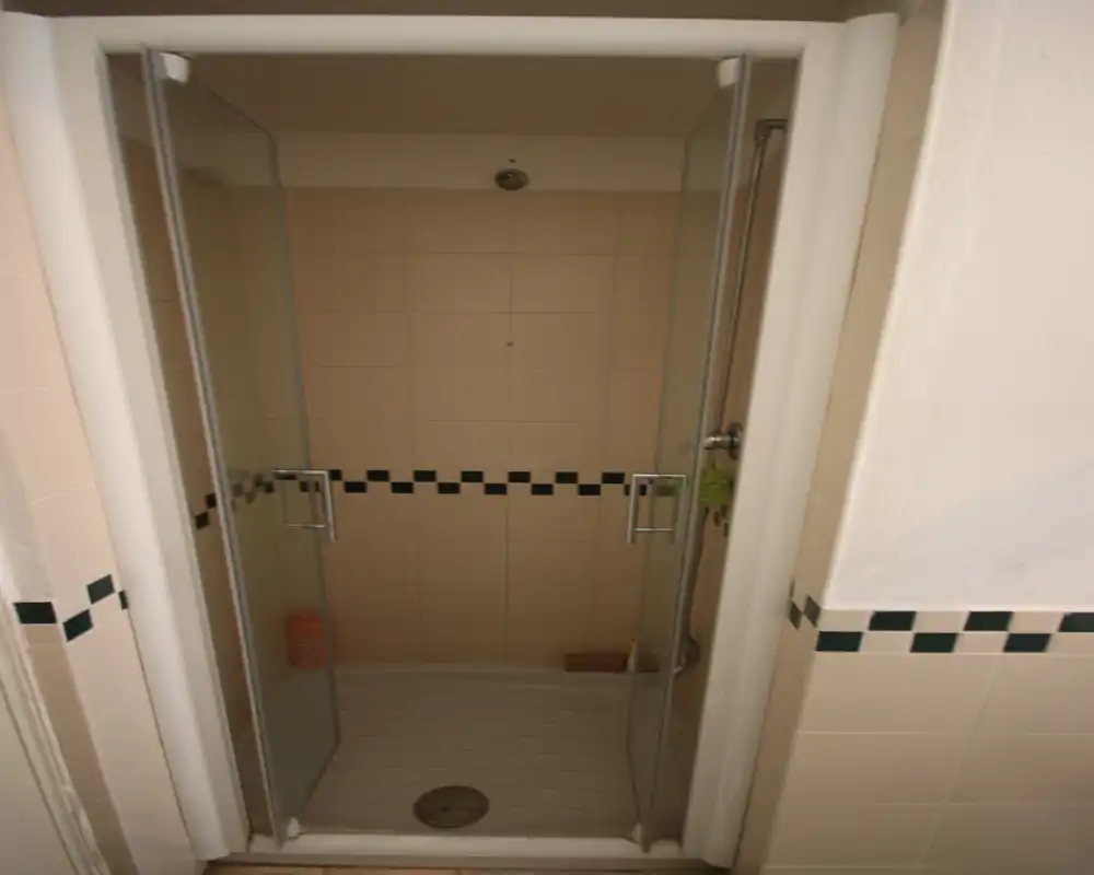 Ducha empotrada con baldosas, puertas correderas de cristal, alcachofa de pared y franja decorativa de azulejos — ideal para un baño funcional.