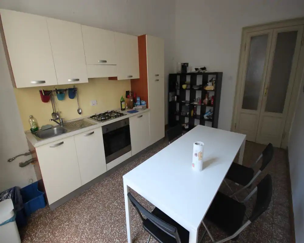 Cocina funcional con horno integrado, fregadero y placa de gas, además de una mesa blanca y sillas plegables — distribución práctica para el uso diario.