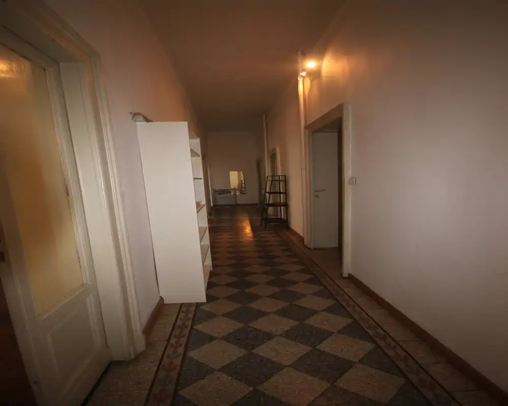 Largo pasillo/entrada interior con suelo de baldosas geométricas, mobiliario mínimo y luz cálida; adecuado como pasillo de edificio o entrada de apartamento.