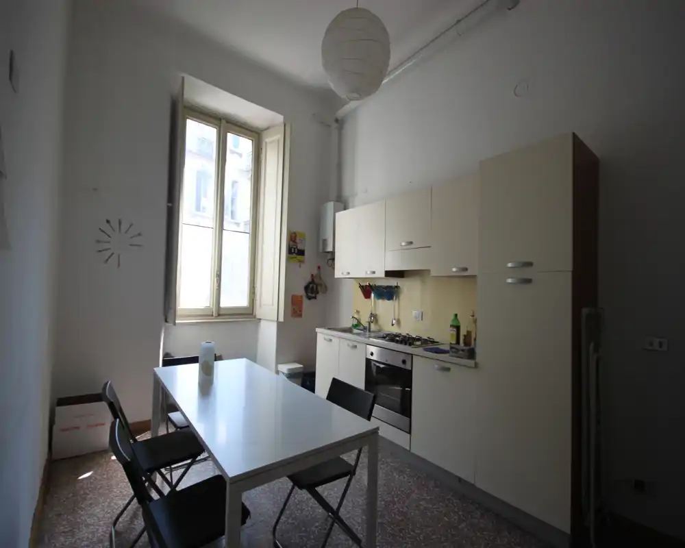 Cocina compacta con armarios empotrados, placa de gas y horno, además de una mesa de comedor sencilla junto a una ventana alta que proporciona luz natural.