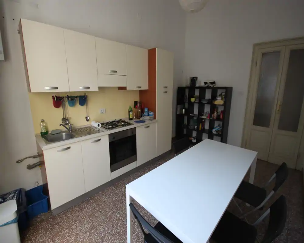 Cocina compacta con muebles lineales, placa de gas y horno, además de una mesa blanca y sillas; funcional y de mobiliario sencillo, adecuada para alquileres cortos.