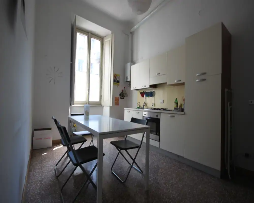 Cocina funcional y luminosa con muebles integrados, horno y mesa de comedor junto a una gran ventana — ordenada y práctica para el uso diario.
