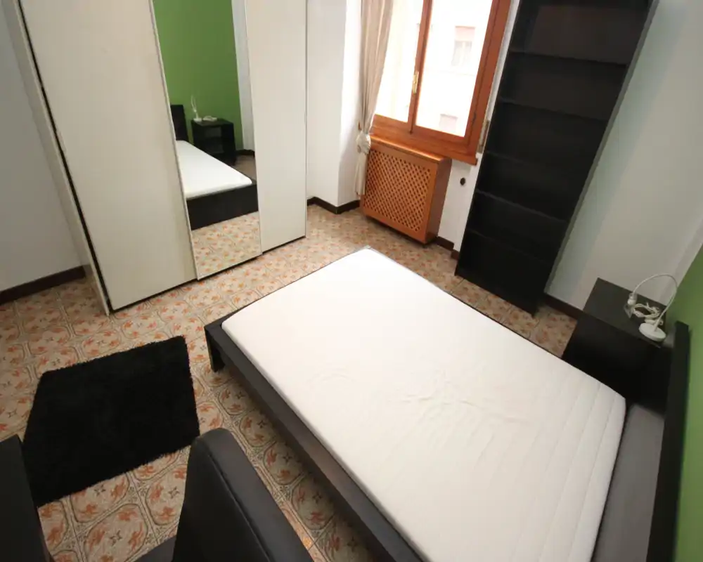 Chambre lumineuse et simplement meublée avec un lit double, une garde-robe miroir, une fenêtre apportant la lumière naturelle et des étagères. Décor sobre et soigné, adapté aux photos d'annonce.
