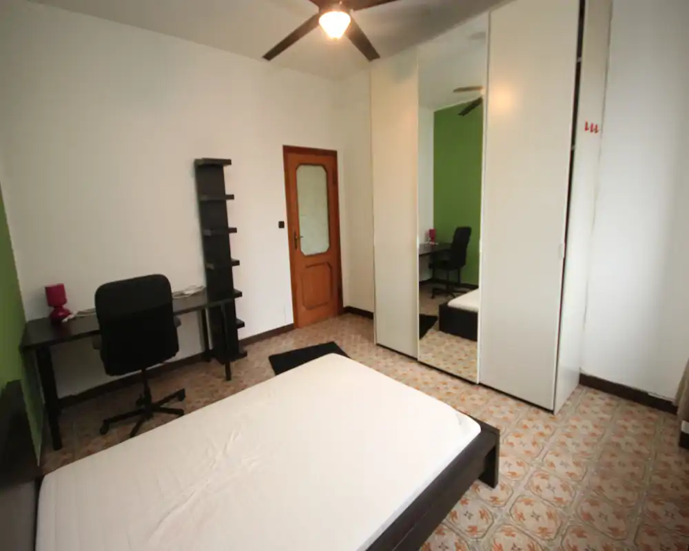 Chambre lumineuse et simple avec un lit double, une armoire miroir et un bureau — agencement soigné et bonne lumière naturelle/au plafond.