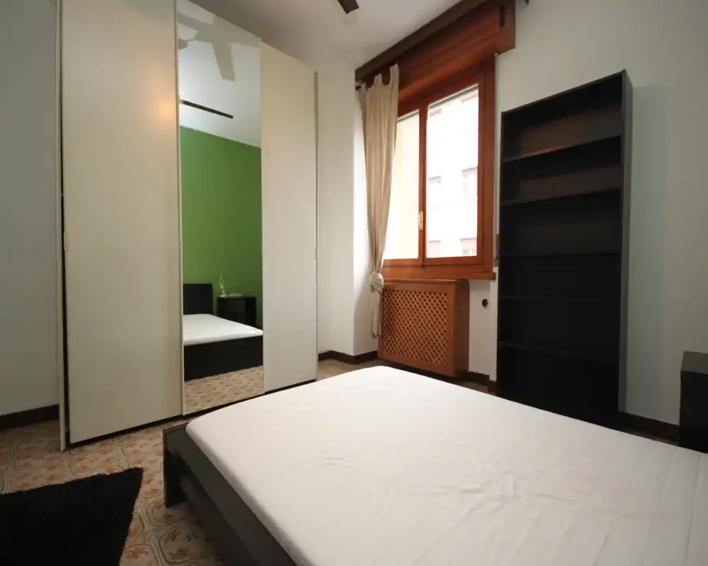Chambre lumineuse et sobrement meublée avec lit bas, armoire à portes miroir et grande fenêtre apportant beaucoup de lumière naturelle.