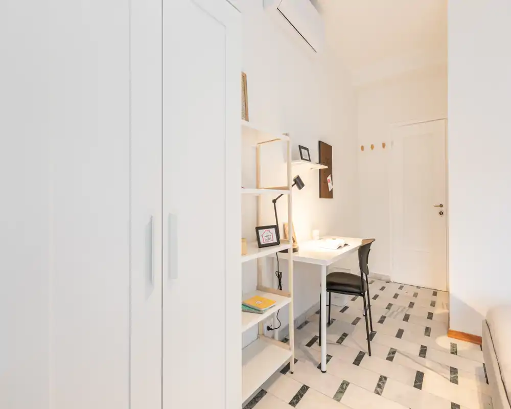Bright, minimal living area with a compact desk and shelving unit; neutral palette and tiled floor create a clean, functional space ideal for remote work or relaxing.