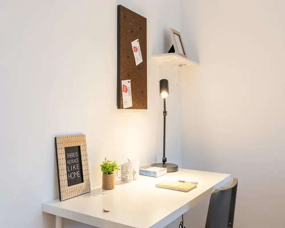 Angolo di lavoro luminoso e minimale con scrivania bianca, lampada da tavolo, stampa incorniciata e piccola pianta — perfetto per concentrarsi nello studio.