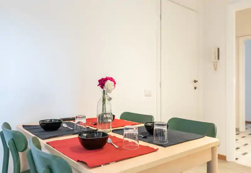 Bright, neatly set dining table with colorful placemats, bowls and a central vase — a compact, welcoming dining area ideal for everyday meals.