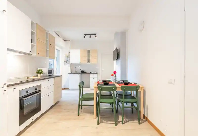 Bright, modern open kitchen with wooden cabinets, built-in oven and a small dining table set for four — well-lit and welcoming for short stays.