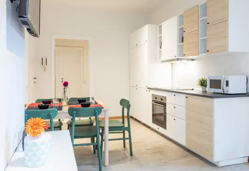 Bright modern kitchen with integrated cabinets, oven and a small dining table set for four; light wood and white finishes create a fresh, welcoming space.