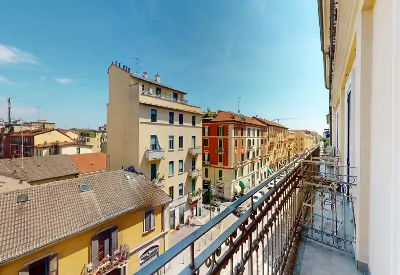 Balcone soleggiato con vista su una via cittadina con edifici storici colorati — perfetto per il caffè mattutino e osservare la vita urbana.