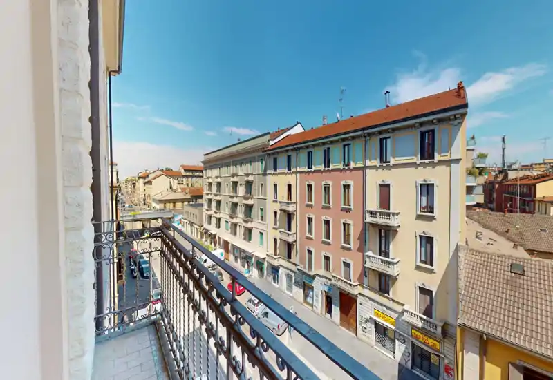 Balcone soleggiato con vista su una via cittadina e condomini di media altezza; perfetto per un caffè mattutino con cielo sereno.