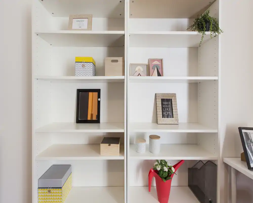 Mensole bianche integrate con scatole decorative, cornici e una pianta — un mobile espositivo ordinato ideale per interni allestiti o come spazio di archiviazione per home office.